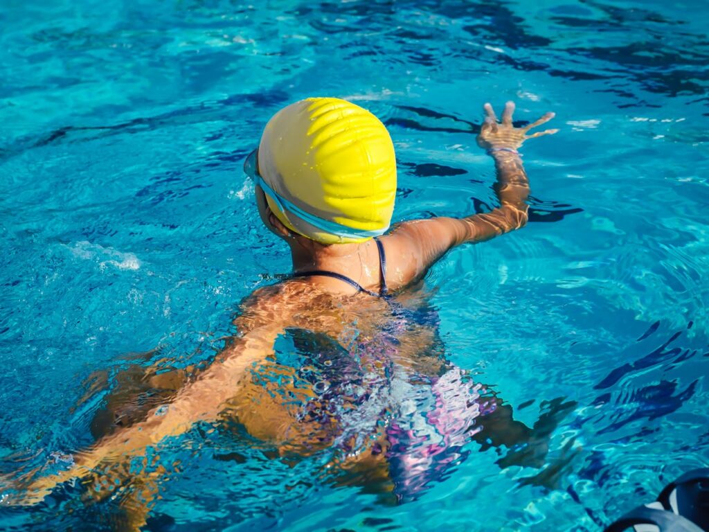 A swimmer wearing a yellow cap enjoying a pool swim captured from the back, highlighting effective technique.